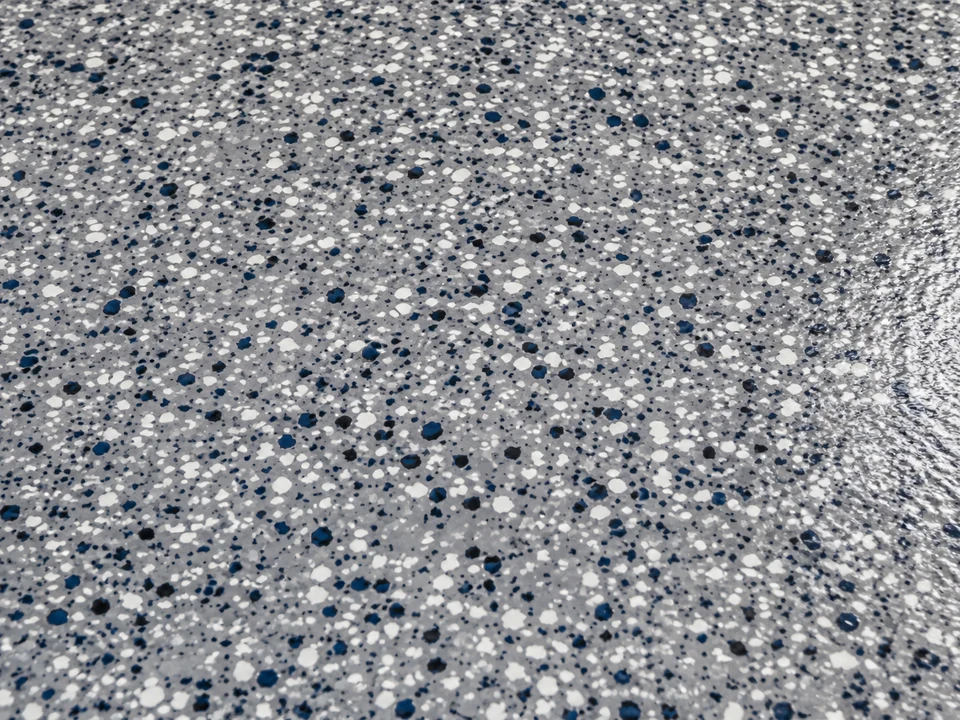 Close-up of a flake epoxy floor finish with white, charcoal, and navy chips under a glossy topcoat